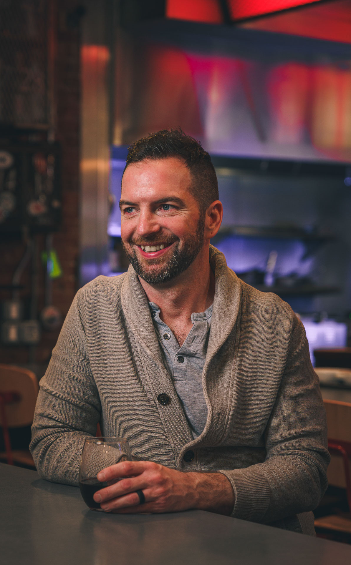 Sean Hellyar sitting at a high top table holding a glass of wine, wearing a sweater